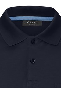 Mörkblå pikétröja med en texturerad krage, två svarta knappar och en ljusblå innerkrage som accent. Innehåller en etikett med "Maerz Muenchen."