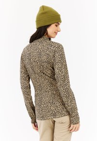 Top de manga larga ajustado en beige con estampado de leopardo negro. Tejido suave con una textura lisa, complementado con un gorro de punto verde.