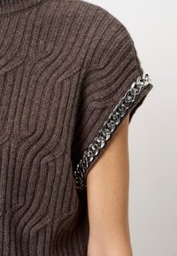 Bruin gebreid top met een textuurgolfpatroon, voorzien van een metallic kettingaccent langs de mouwranden. Glad en aansluitend ontwerp.