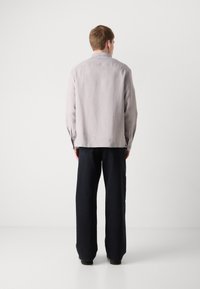 Lichtgrijs overhemd met lange mouwen, een ontspannen pasvorm, details van een rugpas en gecombineerd met losse, donkere broeken. Eenvoudig, minimalistisch ontwerp.