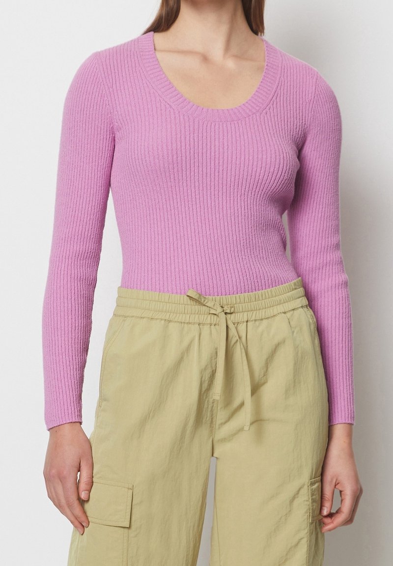 Pull à côtes rose clair avec un col dégagé et des manches longues, associé à un pantalon cargo vert clair avec une taille à cordon.
