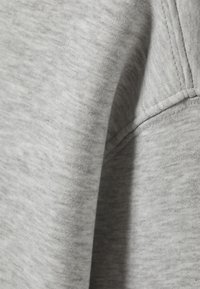 Siva trenirka odjeća s meliranim teksturom, vidljive šavove duž spojeva i mekani, blago pahuljasti površinski sloj.