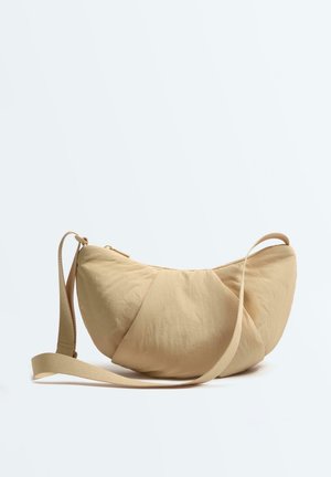 Bež torbica u obliku polumjeseca s podesivim remenom i patentnim zatvaračem, prikazana na bijeloj pozadini.