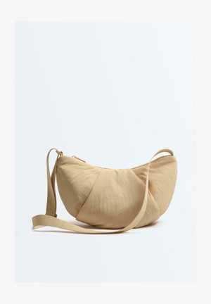 Bež torbica u obliku polumjeseca s podesivim remenom i patentnim zatvaračem, prikazana na bijeloj pozadini.