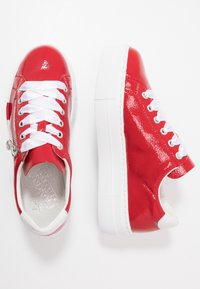 Baskets en cuir verni rouge avec des lacets blancs et une fermeture éclair sur le côté. Semelle en caoutchouc blanc épais et texture lisse et brillante.