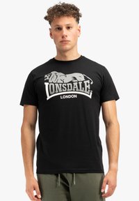 Crna pamučna majica s istaknutim sivim grafičkim prikazom lava i natpisom "Lonsdale London" u podebljanom, zakrivljenom dizajnu. Kratki rukavi.
