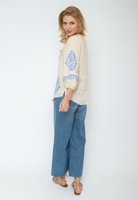 Linnen blouse in beige met blauwe bloemen borduursel, driekwartmouwen. Een paar lichtblauwe wijde jeans en tangekleurde sandalen met bandjes.