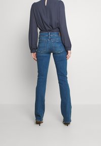 Slim-fit blå jeans med medelhög midja, med bakfickor, knappstängning och subtila sömdetaljer. Inkluderar en mörkgrå blus.