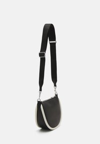 Bolso de hombro de cuero negro con un acento blanco a lo largo del borde. Cuenta con una correa ajustable negra y herrajes de plata. Forma de media luna.