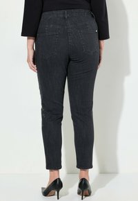 Jeans skinny de mezclilla negra de cintura alta, con bolsillos traseros y un leve desgaste a lo largo de las piernas. Corte entallado.
