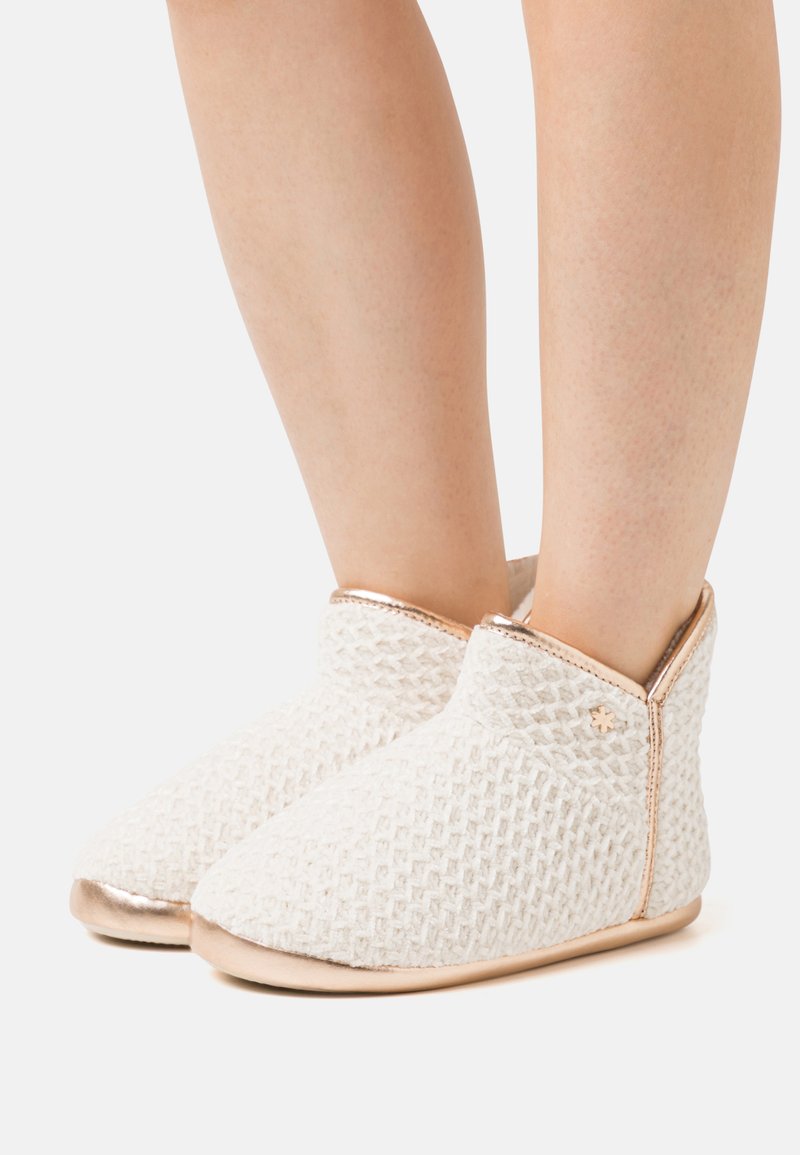 White textured slippers with a geometric pattern, featuring a gold accent at the ankle and a soft, flexible sole.