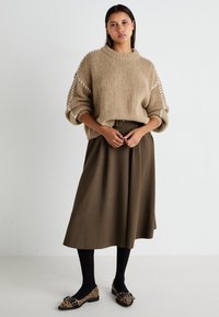 Beige strikket genser med overdimensjonerte ermer, paret med en mørkebrun midiskjørt, sorte strømpebukser og leopardmønstrede flate sko.