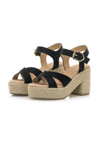 Sandalias de plataforma negras con suela de estilo espadrille texturizada, que presentan tiras entrecruzadas y un acento de hebilla dorada en la correa del tobillo.