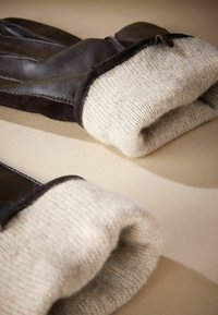 Læderhandsker med en mørkebrun yderflade og beige strikkede manchetter, der fremviser en blød tekstur og lagdelt design.