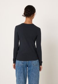 Pikakarvaline, tumehall särk, mis on valmistatud siledast kangast. Omadusteks on ümar kaelus ja istuv siluett, mida on kombineeritud helesiniste, lahtise lõikega teksadega.