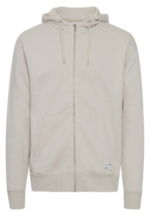 Hanorac cu fermoar de culoare bej deschis, cu glugă, buzunare frontale, mansete și tiv din bumbac cu model de țeavă. Fabricat dintr-un material moale, are șnururi ajustabile și un patch cu logo.