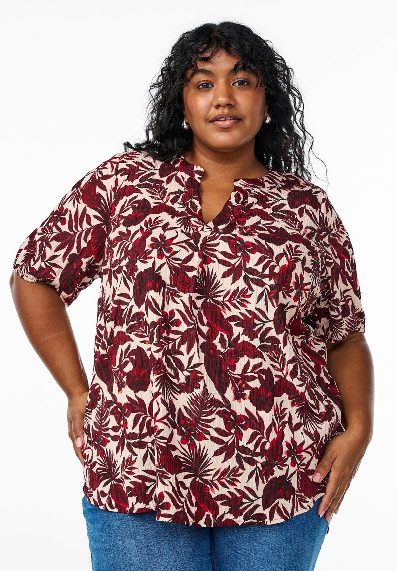 Blusa de manga corta en crema claro con un patrón floral en rojo y marrón. Presenta un escote en V, tejido texturizado y un ajuste relajado.