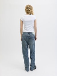 White short-sleeve t-shirt with a black neckline, paired with loose, light blue denim jeans featuring back pockets and a label on the waistband.