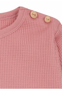 Waffle-Strickoberteil in sanftem Rosa mit Rundhalsausschnitt, ausgestattet mit zwei Holzknöpfen an der Schulter für zusätzlichen Detail.