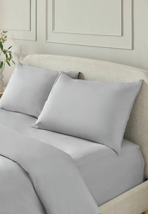 Beiges Polsterbett mit hellgrauem Spannbettlaken, zwei Kissen und passender grauer Bettdecke in einem minimalistischen Schlafzimmer.