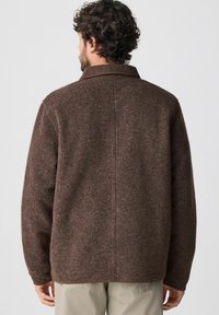 Braune Wolljacke mit weicher Textur, ausgestattet mit einem Reverskragen und sichtbaren Nähten, von hinten gezeigt.