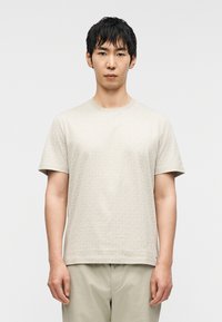 Μπεζ κοντομάνικο T-shirt με διακριτικό γεωμετρικό μοτίβο, σχέδιο με στρογγυλή λαιμόκοψη και μαλακή υφή υφάσματος, συνδυασμένο με ανοιχτόχρωμο παντελόνι.