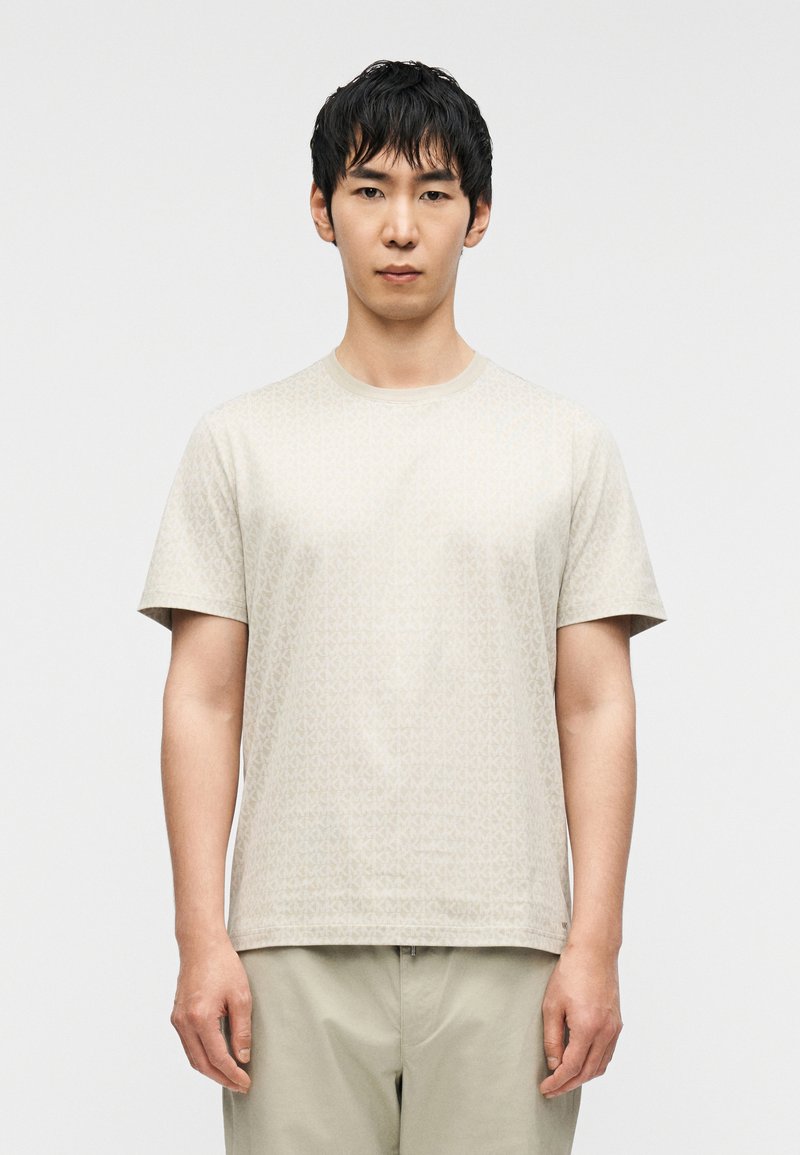 Μπεζ κοντομάνικο T-shirt με διακριτικό γεωμετρικό μοτίβο, σχέδιο με στρογγυλή λαιμόκοψη και μαλακή υφή υφάσματος, συνδυασμένο με ανοιχτόχρωμο παντελόνι.