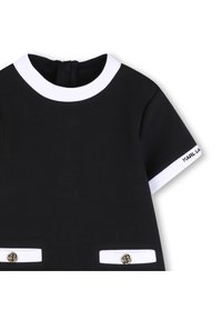 Μαύρο φόρεμα με κοντά μανίκια, λευκό γιακά και περιθώριο στα μανίκια, με δύο εμπρόσθιες τσέπες με χρυσά κουμπιά και λογότυπο στο μανίκι.