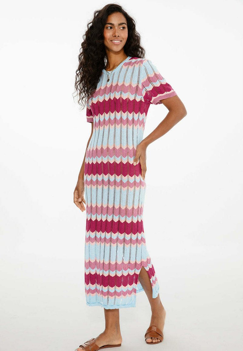 Dzianinowa sukienka midi z wzorem w zygzak w jasnym niebieskim, różowym i burgundowym kolorze, krótki rękaw i boczne rozcięcia dla swobody ruchów.