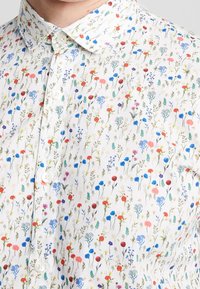 Camisa blanca de botones con un patrón floral en varios colores, incluyendo rosa, azul y naranja. Tela suave con un cuello estándar.