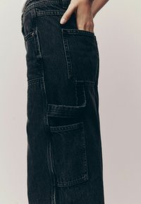 Pantaloni din denim negri cu o croială relaxată, având mai multe buzunare supradimensionate și cusături pronunțate pentru textură și durabilitate.
