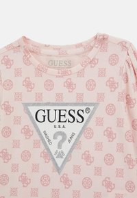 T-shirt rosa chiaro realizzato in cotone biologico, caratterizzato da un motivo testurizzato di loghi, una grafica a triangolo argentato con "GUESS" e colletto a girocollo.
