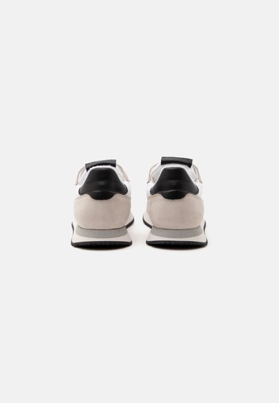 Paire de baskets beiges et blanches avec empiècements noirs au talon, vue de dos sur fond blanc uni.