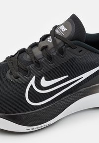 Chaussure de course Nike Zoom Fly noire avec une tige texturée, un logo blanc et une semelle blanche contrastante avec des détails antidérapants.