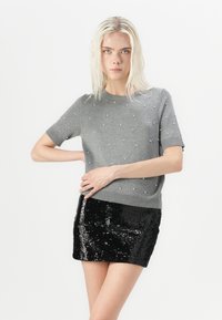Gray short-sleeve sweater with pearl accents; paired with a shiny black sequin mini skirt. Smooth texture; fitted design.