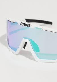 Zonnebril met een wit frame en zwarte accenten, reflecterende lenzen in tinten blauw en paars, hoekig ontwerp met een sportieve esthetiek.