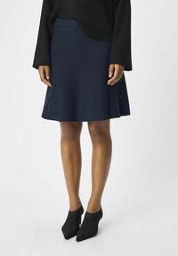Falda de campana azul marino con una textura suave, combinada con botines negros de punta. El conjunto se completa con una camiseta negra de manga larga con canalé.