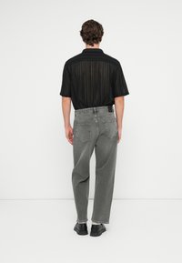 Juodas trumpas rankovėmis marškinėliai su vertikaliomis juostelėmis, derinami su pilkais plačiais džinsais. Aprangą papildo juodi batai, matomi iš nugaros.