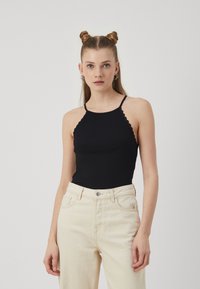 Black ribbed tank top with scalloped edges, paired with high-waisted off-white jeans, featuring a smooth texture and minimalistic design.