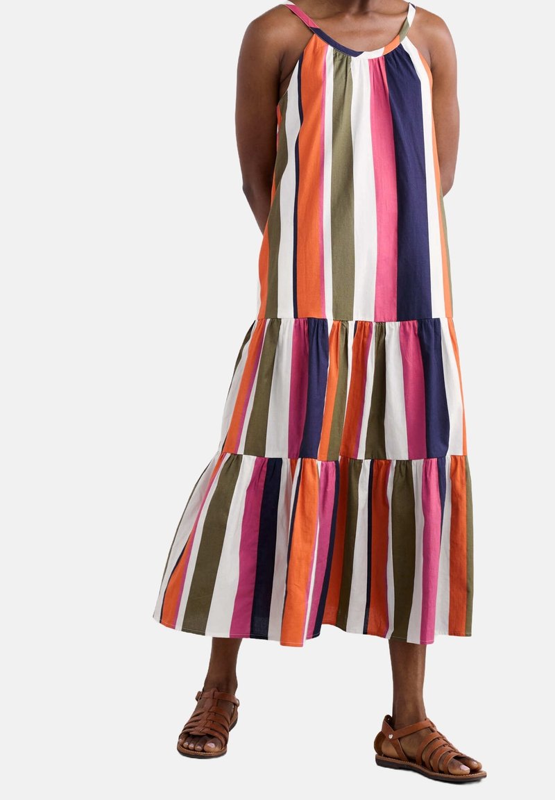 Femme portant une robe sans manches, longueur cheville, avec des rayures verticales orange, marine, olive, blanc et rose, associée à des sandales marron.