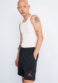 Sorte atletiske shorts med et pink Jumpman-logo, elastisk talje og sidelommer, parret med en hvid tanktop. Glat bomuldsstruktur.