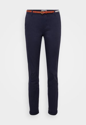 Meripihkashousut slim-fit-mallissa, joissa on ruskea nahavyö pyöreällä metallisoljella ja käärityt lahkeet nilkoissa. Silkkinen puuvillakangas.