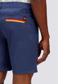 Pantaloni corti blu navy con una texture liscia, dotati di una tasca posteriore con una zip multicolore e un piccolo tag con logo vicino alla zip.