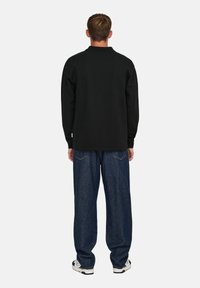Sudadera negra de manga larga con cuello de canalé, combinada con unos vaqueros de denim azul holgados. Presenta detalles en blanco y un diseño de ajuste relajado.