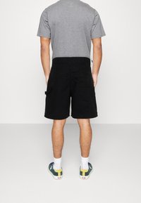 Mustat cargo-shortsit, joissa on rento leikkaus, sivutaskut ja teksturoitu pintakuvio, yhdistettynä harmaaseen lyhythihaiseen T-paitaan.