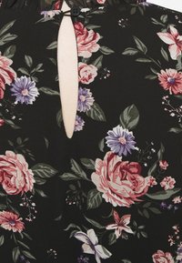 Tissu noir à motif floral avec de grandes roses roses, des fleurs de lavande et des feuilles vertes ; comprend un détail d'ouverture en forme de trou de serrure avec une fermeture à bouton.