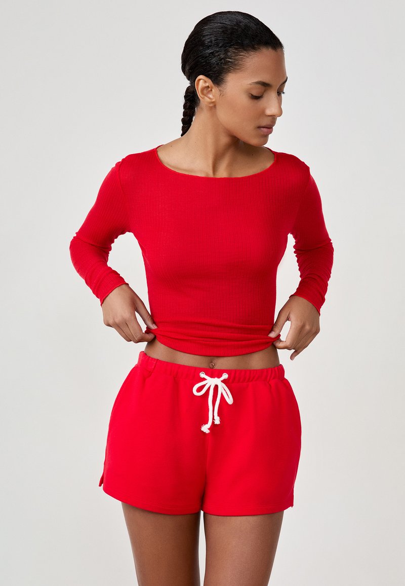 Rode geribbelde top met lange mouwen gecombineerd met rode shorts met koord. De outfit heeft een aansluitend ontwerp met een zachte textuur.
