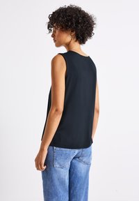 Top nero senza maniche con scollatura rotonda e texture liscia, abbinato a jeans azzurri chiari a vita alta con tasche posteriori.