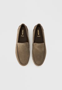 Paire de mocassins marron en daim sans lacets avec coutures apparentes et inscription « GEOX Respira » à l'intérieur sur un fond blanc uni.