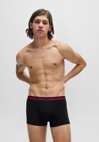 Schwarze Baumwoll-Boxershorts mit einem roten elastischen Bund, der mit "HUGO" Branding versehen ist. Glatte Textur, eng anliegendes Design. Geeignet für den täglichen Gebrauch.